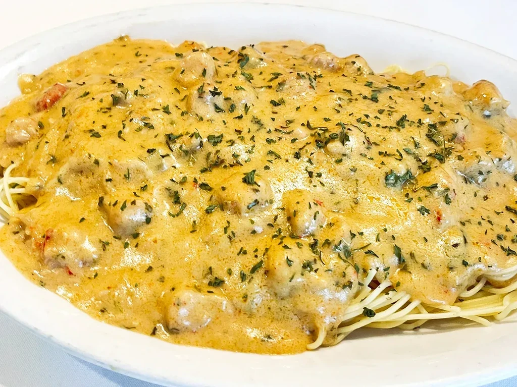Spaghetti with creamy golden-orange sauce, meat chunks, and green herbs.