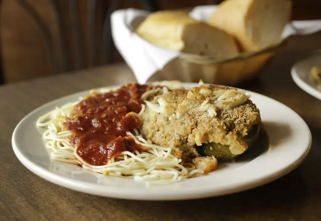 A plate of spaghetti and a stuffed pepper on a wooden table.