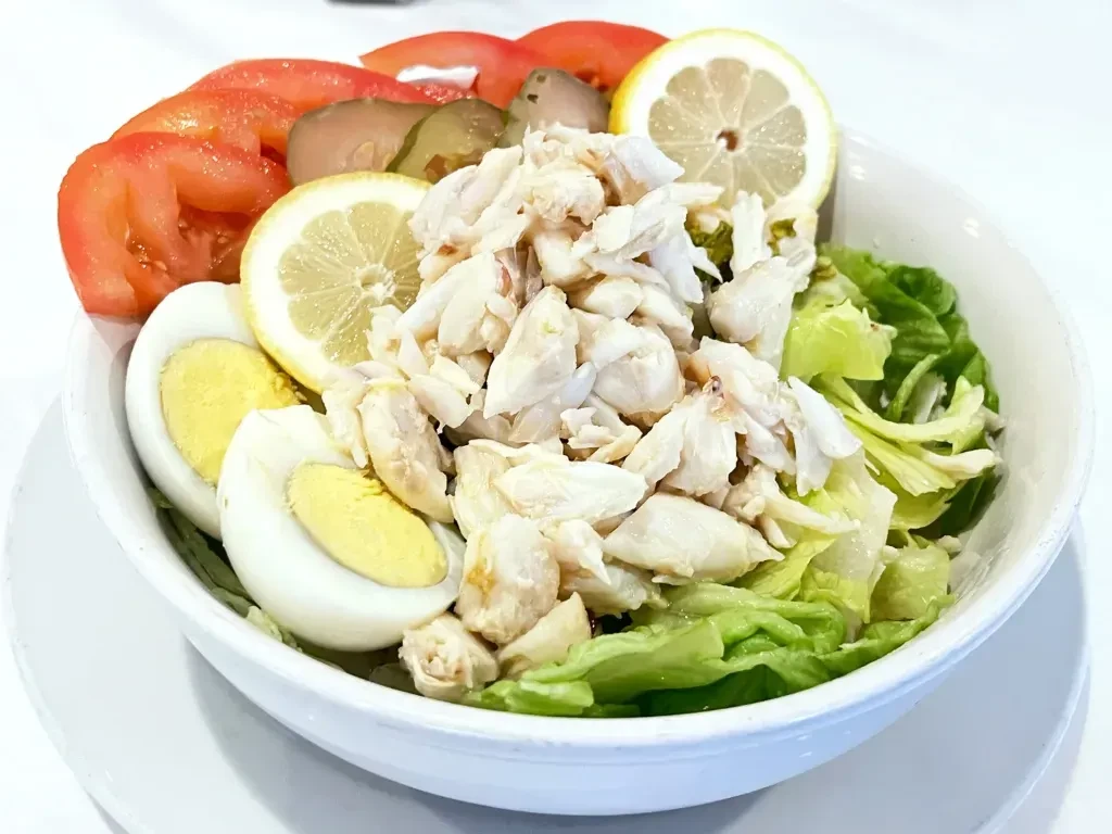 Fresh crab salad with lettuce, tomato, egg, lemon slices, and pickles.
