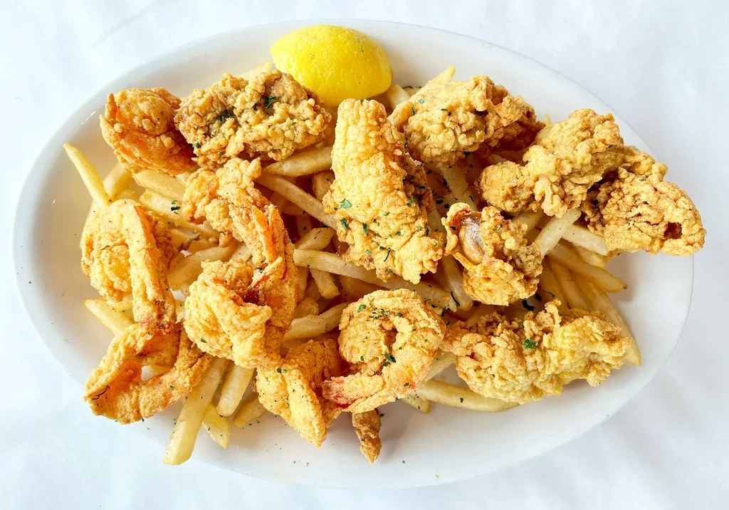 White plate piled high with fried seafood, french fries, and lemon.