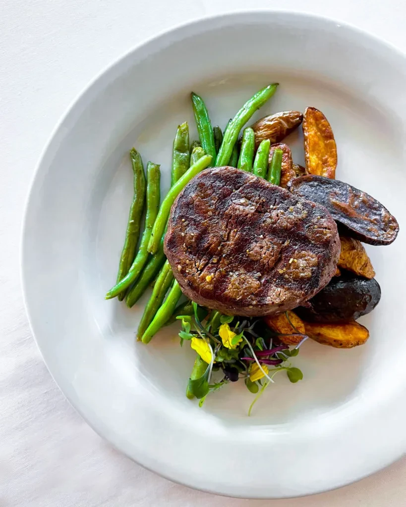 Grilled steak, string beans, roasted potatoes, and microgreens on a plate.