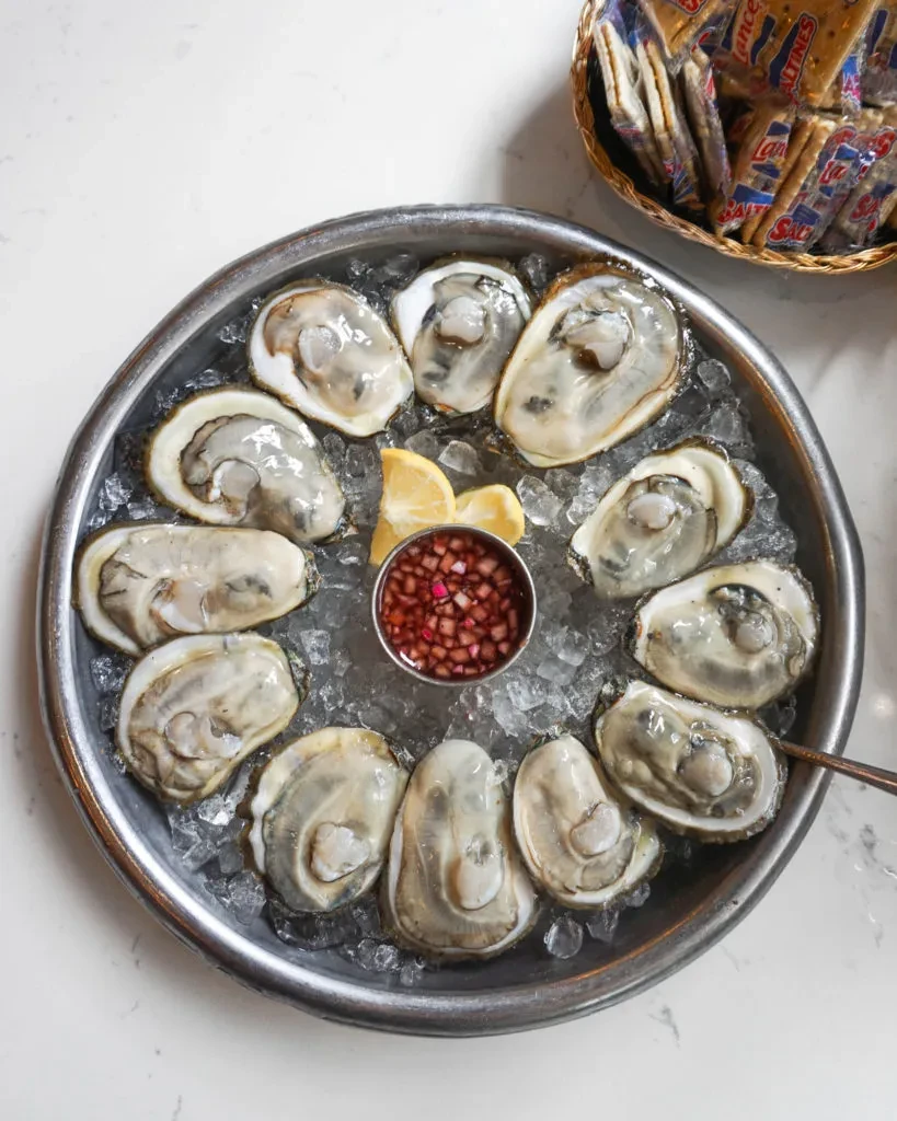 Dozen shucked oysters on ice with mignonette, lemon, and crackers.