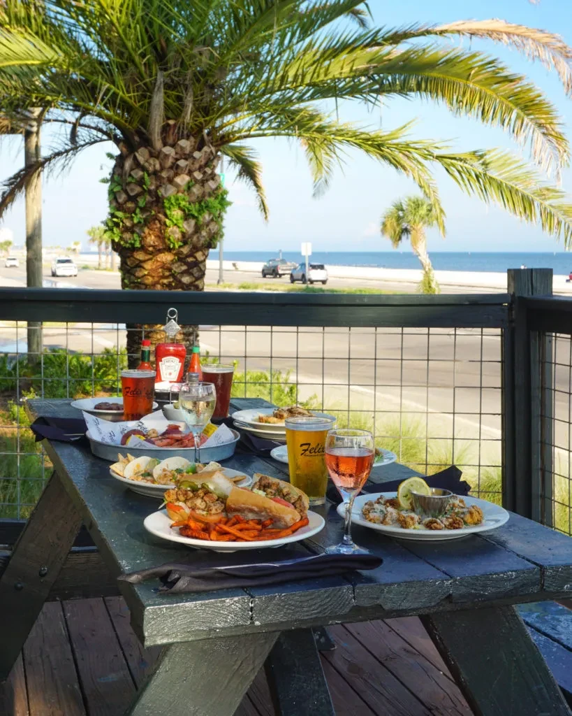 Picnic table laden with fried seafood, beer, and wine by the ocean.