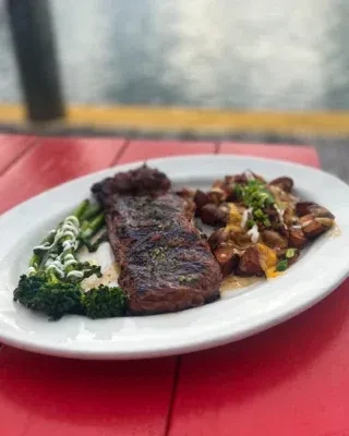 Grilled steak, broccoli, and cheesy potatoes on a white plate outdoors.