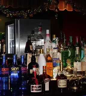 Dimly lit bar counter displaying a wide variety of liquor bottles.