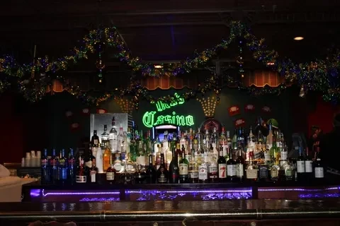 Dimly lit bar with purple-lit liquor bottles and "The Casino" neon sign.