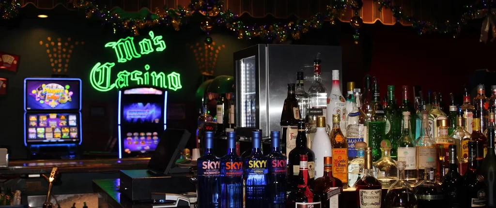 Dimly lit bar counter with bottles, slot machines, and "Mo's Casino" neon sign.