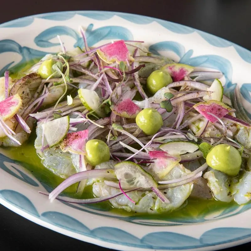 Vibrant ceviche or aguachile with sliced seafood, green sauce, and colorful toppings.