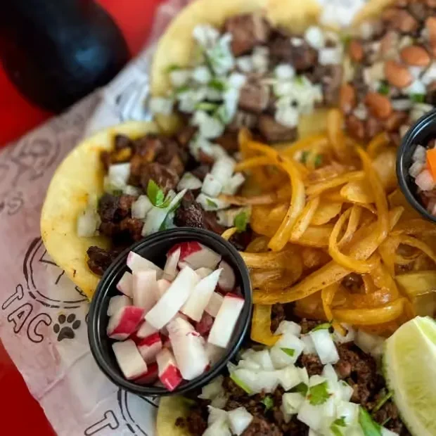 Platter of soft-shell tacos with meat, bean, radishes, salsa, and lime.