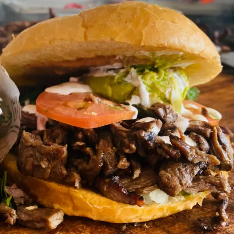 Overflowing torta with shredded meat, guacamole, tomato, and white sauce.
