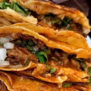 Crispy, golden-brown tacos stacked with shredded meat, onions, and cilantro.