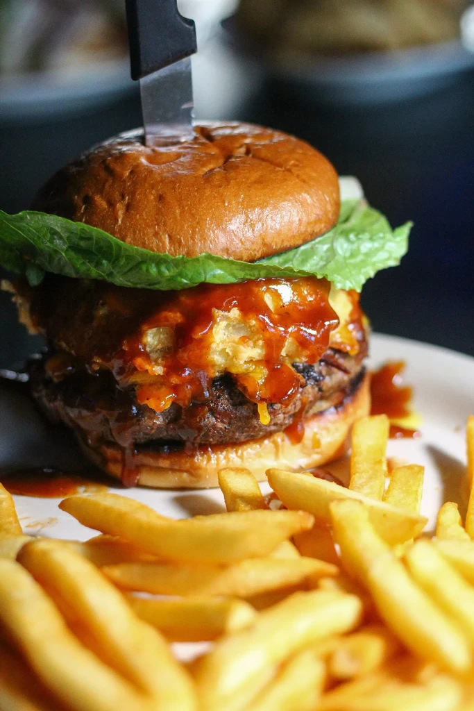 Brioche burger with lettuce, crispy onions, sauce, knife, and fries.