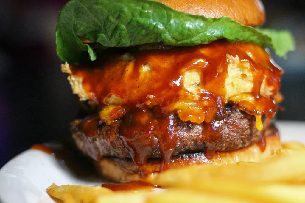 Gourmet burger with beef patty, melted cheese, dripping sauce, fries.