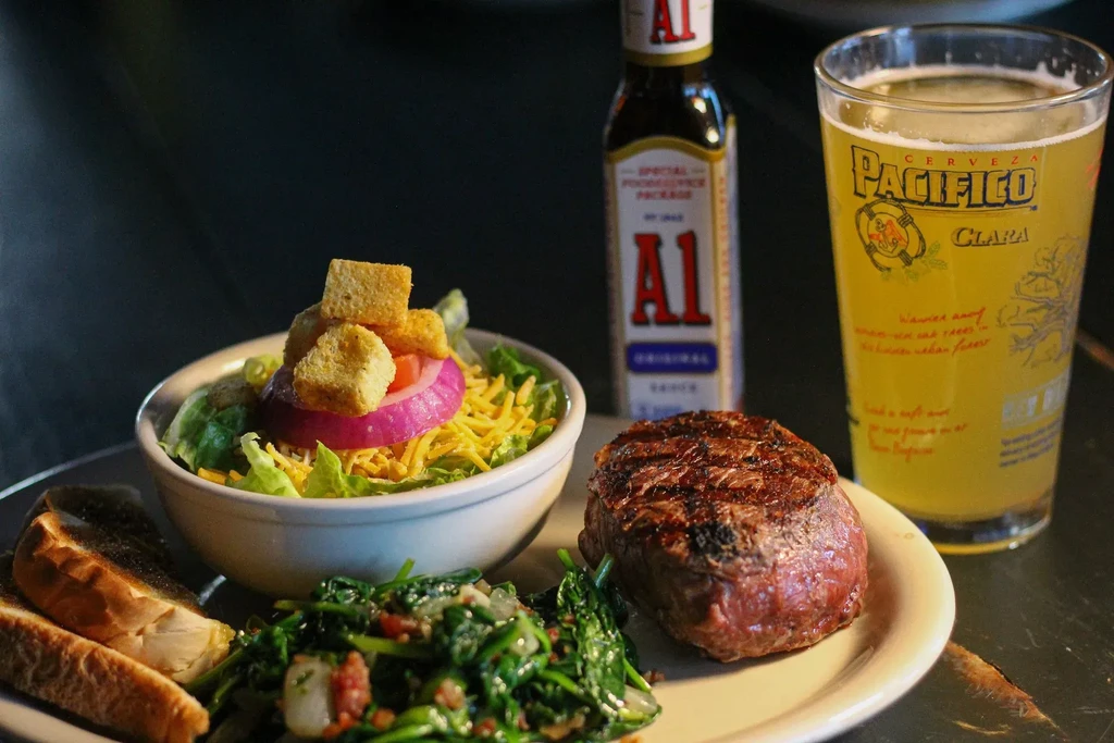 Grilled steak, green vegetables, salad, Pacifico beer, and A1 sauce.