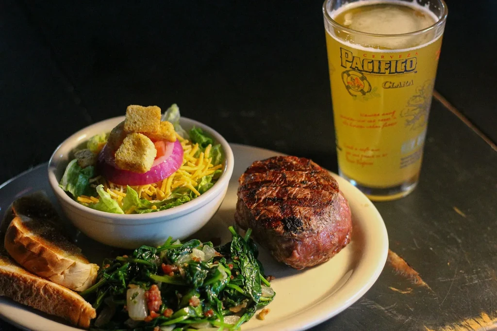 Grilled steak dinner with salad, greens, bread, and Pacifico beer.