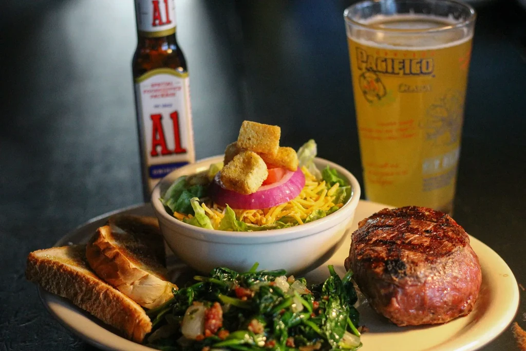 Grilled steak meal with sautéed greens, garden salad, and bread.