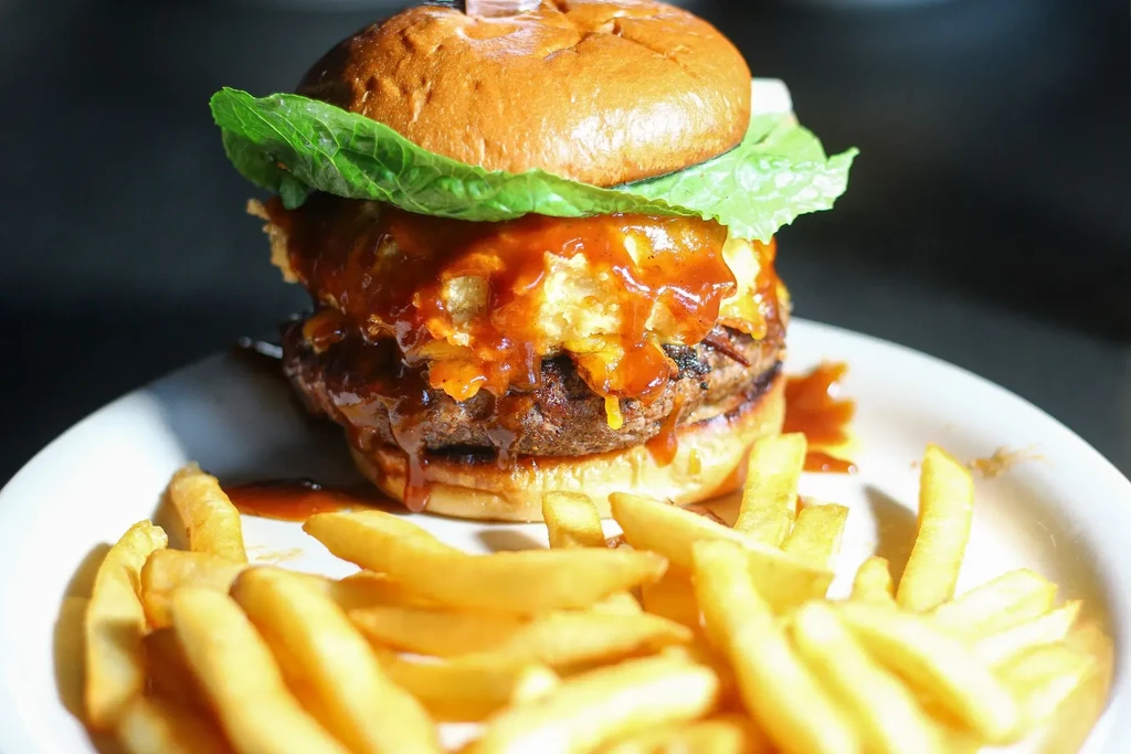 Large double patty burger with red sauce, crispy elements, and fries.