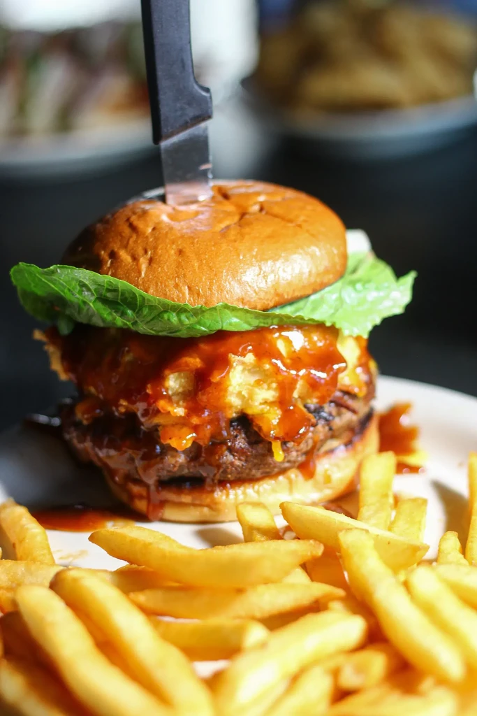Gourmet burger, knife-skewered, with dripping sauce and golden fries.