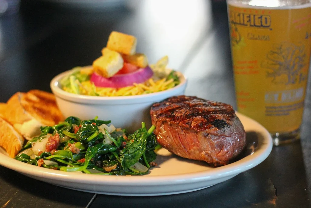 Grilled medium-rare steak, sautéed greens, salad, and a glass of beer.