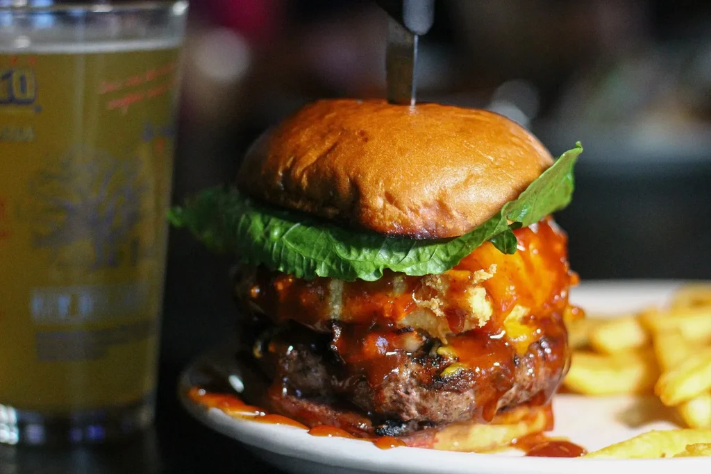 Towering double-patty burger secured with a knife, fries, beer.