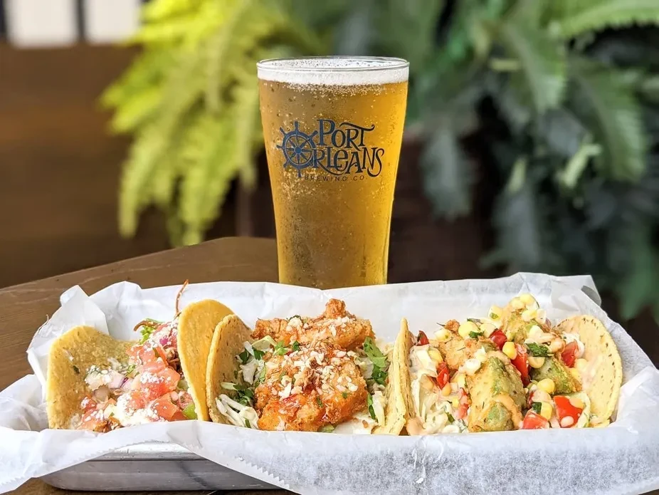 Three varied tacos and cold Port Orleans beer on wooden table.