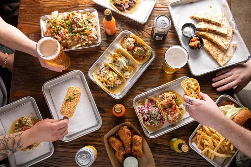 High-angle view of hands reaching for nachos, tacos, wings, and beer.
