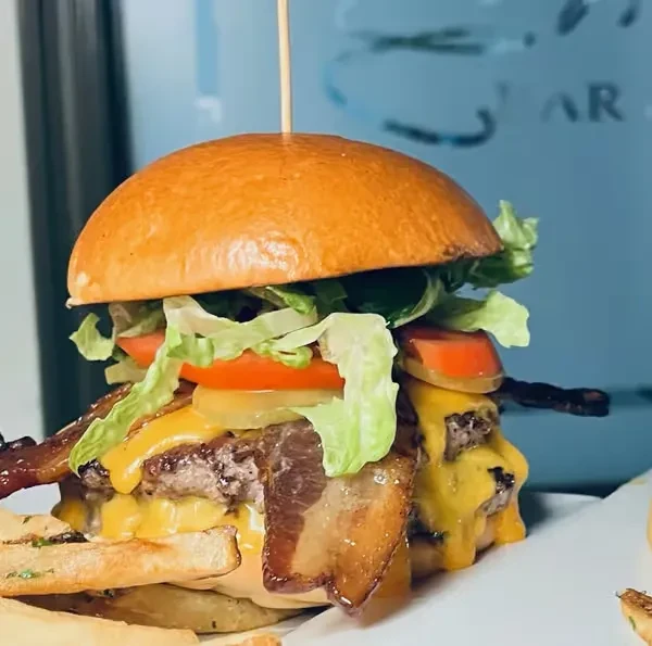 Stacked burger with beef patties, melted cheese, bacon, and fries.