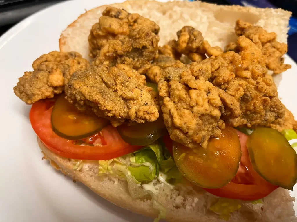 Close-up of golden-brown fried sandwich with lettuce, tomato, pickles.