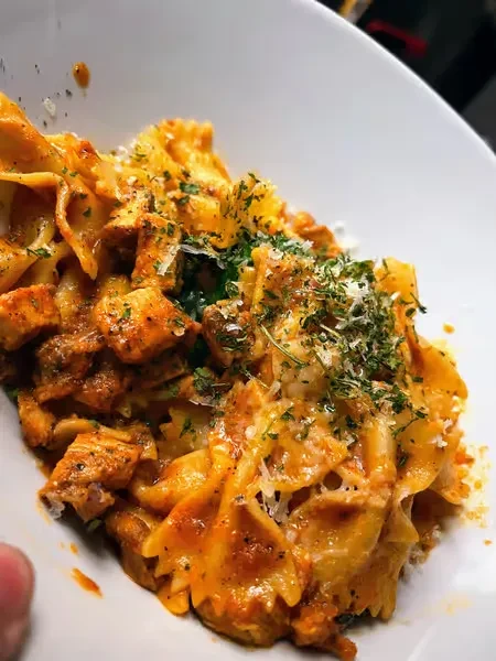 Farfalle pasta with chicken, tomato sauce, fresh herbs, and grated cheese.
