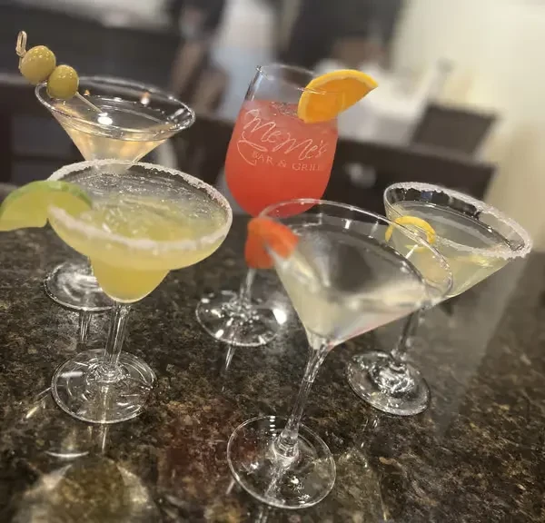 Close-up of five garnished cocktails, one glass branded "Meme's Bar & Grill."