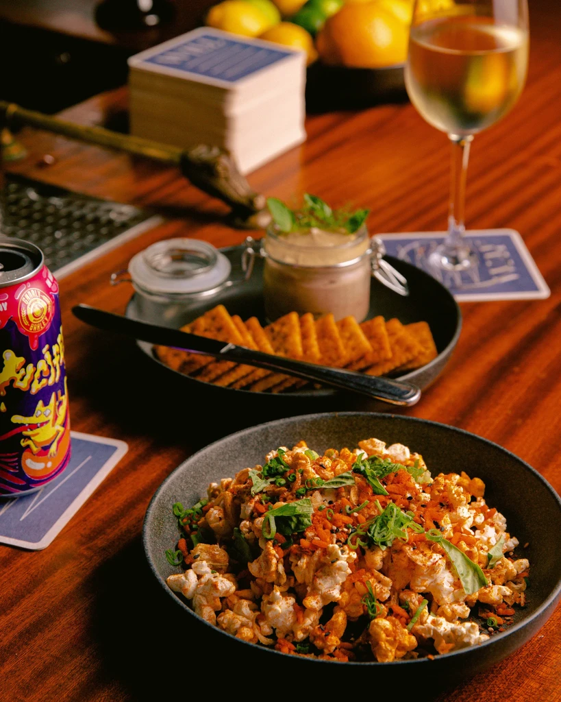 Gourmet popcorn, pâté, crackers, wine, and drink on a dark wooden table.