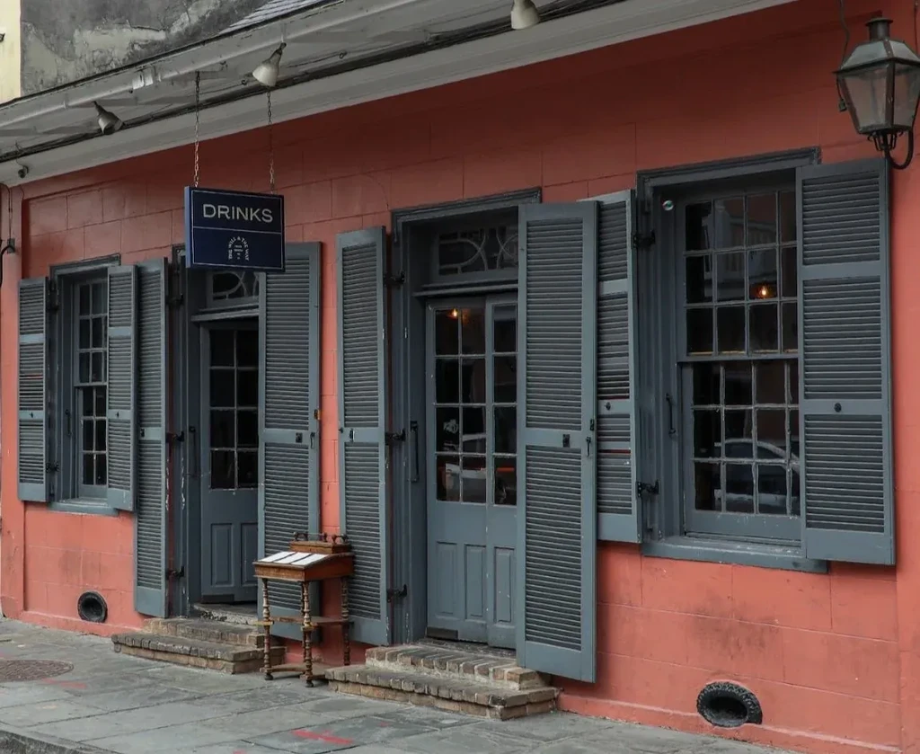 Old reddish-orange building with gray shutters and a "DRINKS" sign.