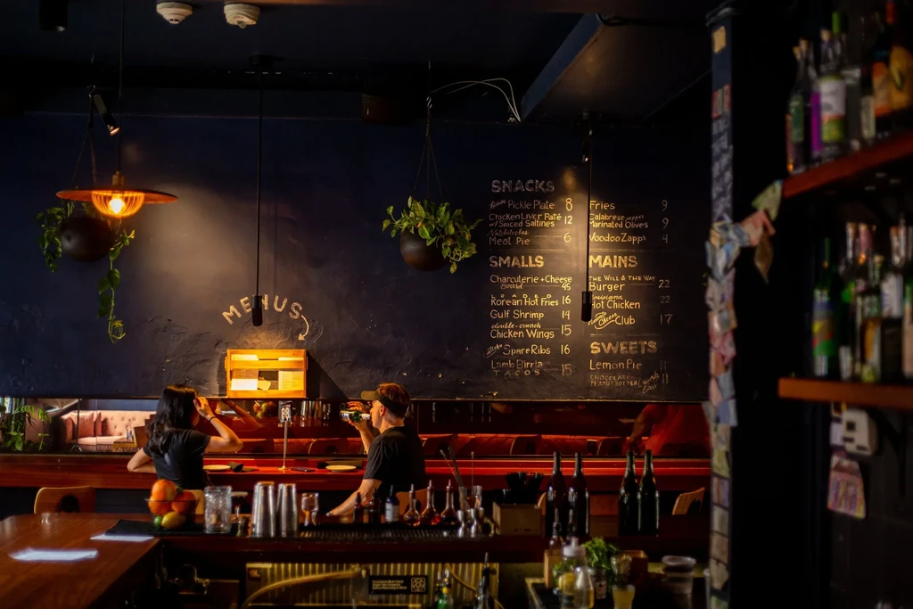 Dimly lit stylish bar interior with a wooden counter and chalkboard menu.