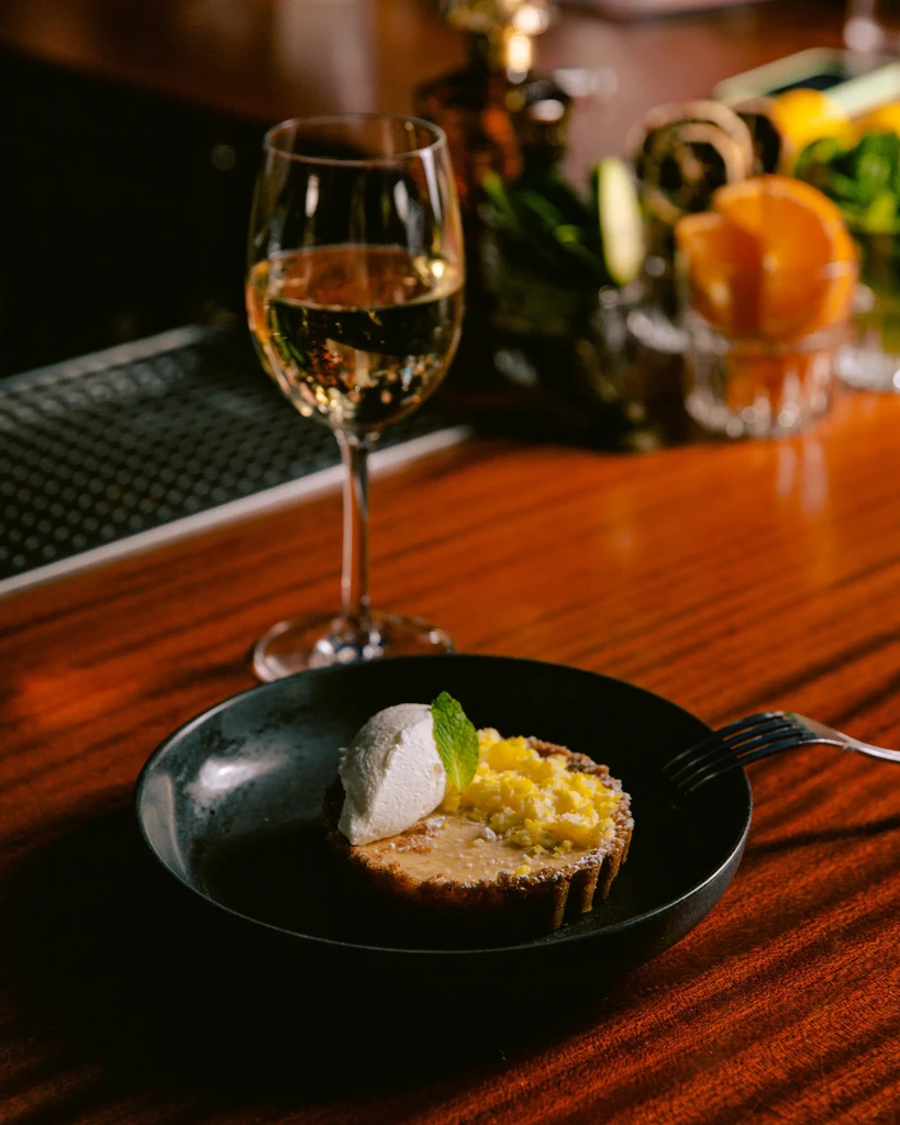 Close-up of a golden tart with cream, mint, and white wine.
