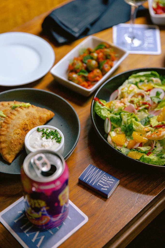 Pastry, shrimp salad, soda, and olives on a wooden table.