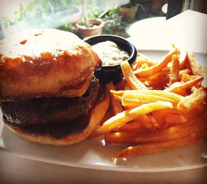 A hearty burger, golden fries, and dipping sauce on a white plate.