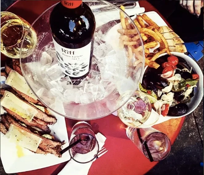 Chilled white wine, sliced meat, and mussels on a red table.