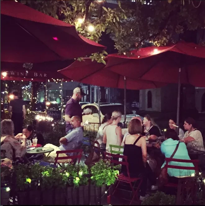 Lively outdoor wine bar patio at night with patrons and string lights.