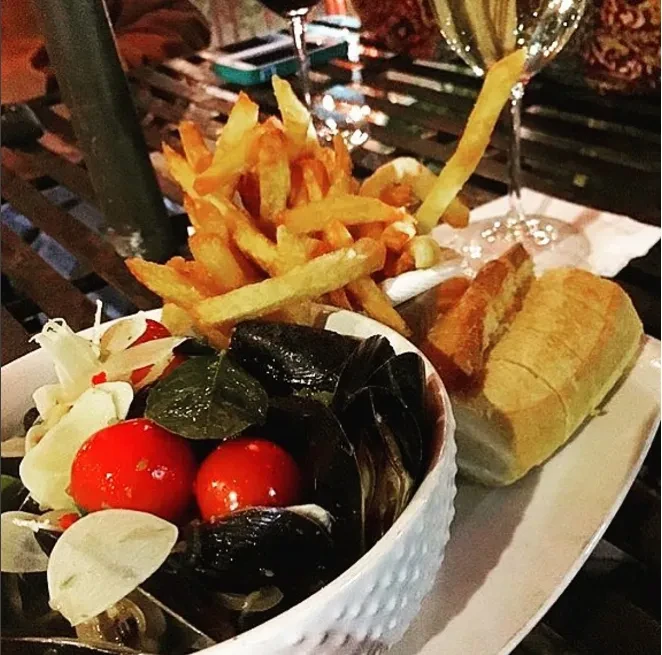 Mussels, french fries, and baguette served with wine at a restaurant.