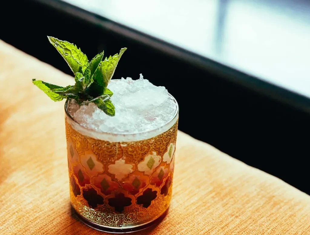 Amber cocktail with crushed ice and mint in a mosaic-patterned glass.