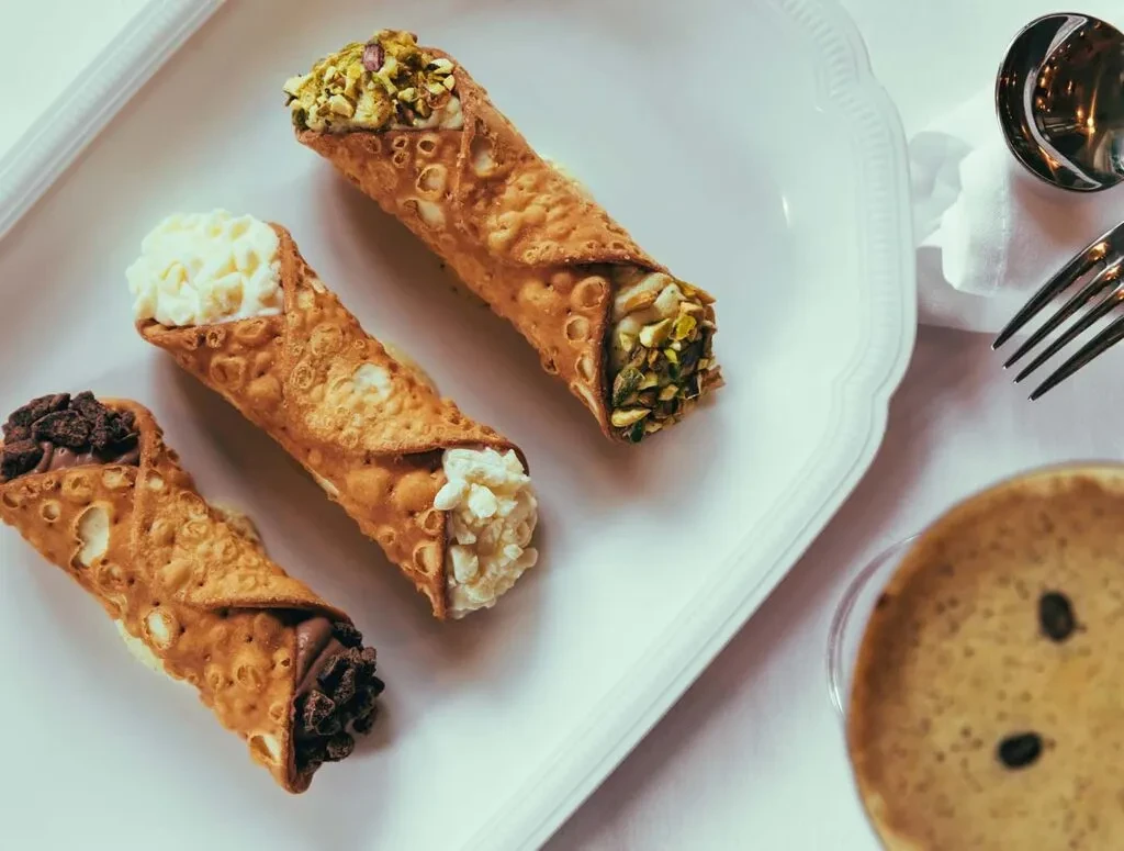 Three cannoli with various fillings, cutlery, and a drink.