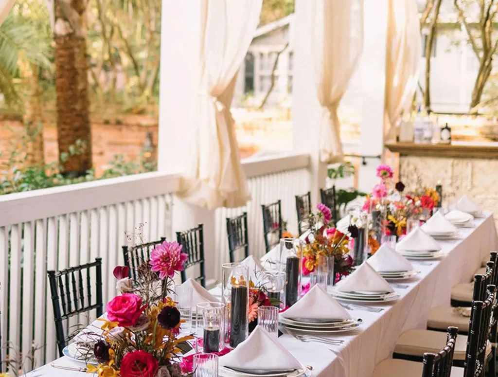 Beautifully set outdoor dining table with vibrant flowers and black chairs.