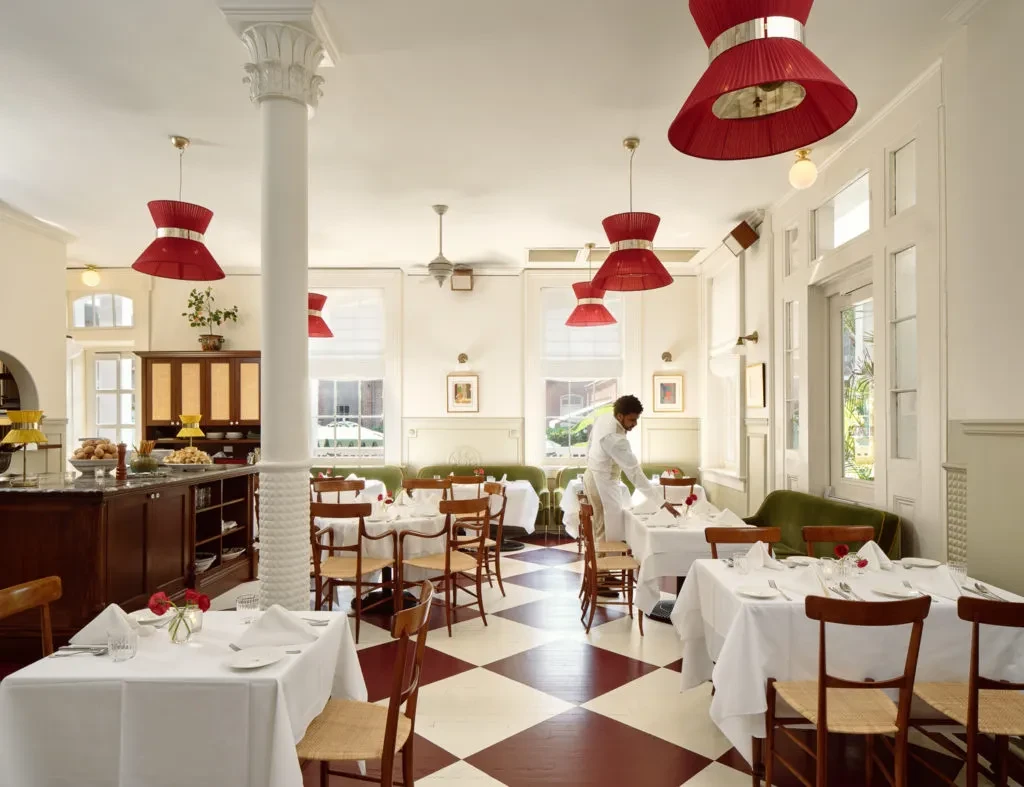 Server adjusts table in elegant restaurant with red checkered floor, red lamps.
