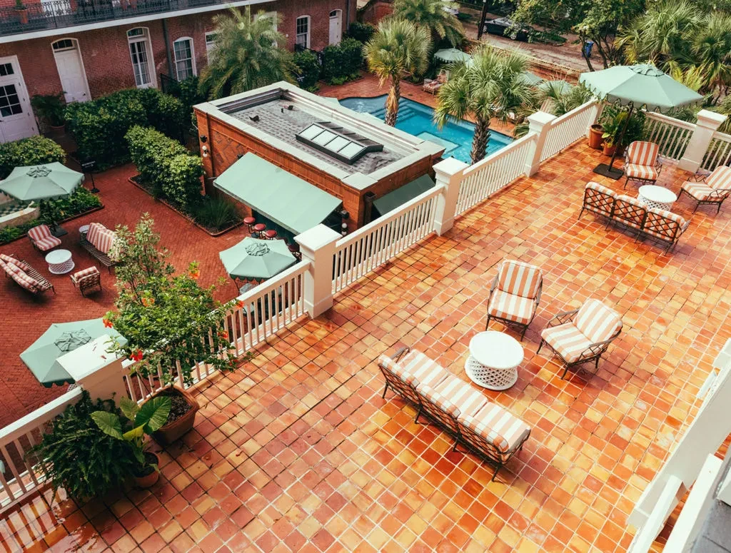 Aerial view: Terracotta patio, colorful umbrellas, striped seating, lush plants, pool.