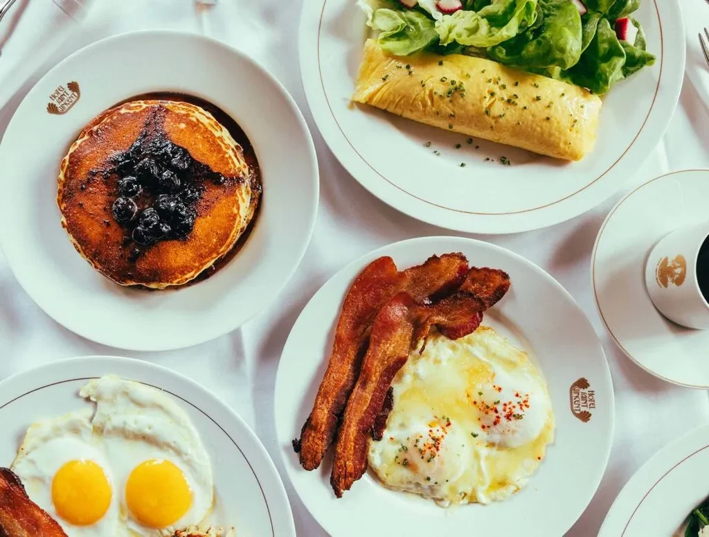 Various Hotel Saint Vincent breakfast dishes: pancakes, omelet, fried eggs, bacon.