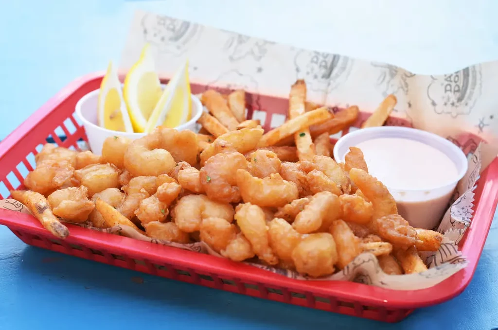 Fried shrimp and fries in red basket, with lemon and pink sauce.