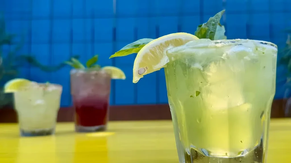 Green drink with lemon and basil, two blurred, on yellow surface.