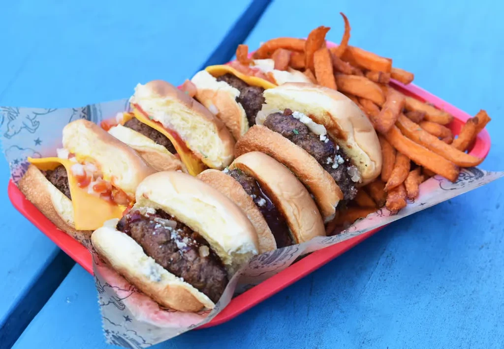 Variety of mini burgers and sweet potato fries on red tray.