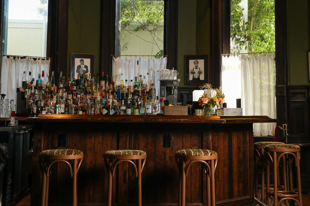 Dark wooden bar counter with liquor bottles, stools, and garden view.