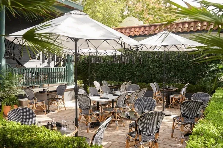 Mediterranean-style outdoor dining with white tables, umbrellas, and green plants.